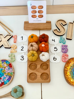Set of six small felt pumpkins in autumn colors on wooden tray with number cards and pumpkin counting flash card