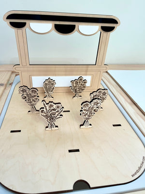 Laser-cut wooden flower bouquets displayed on a small stand with a scalloped canopy on a light wood base