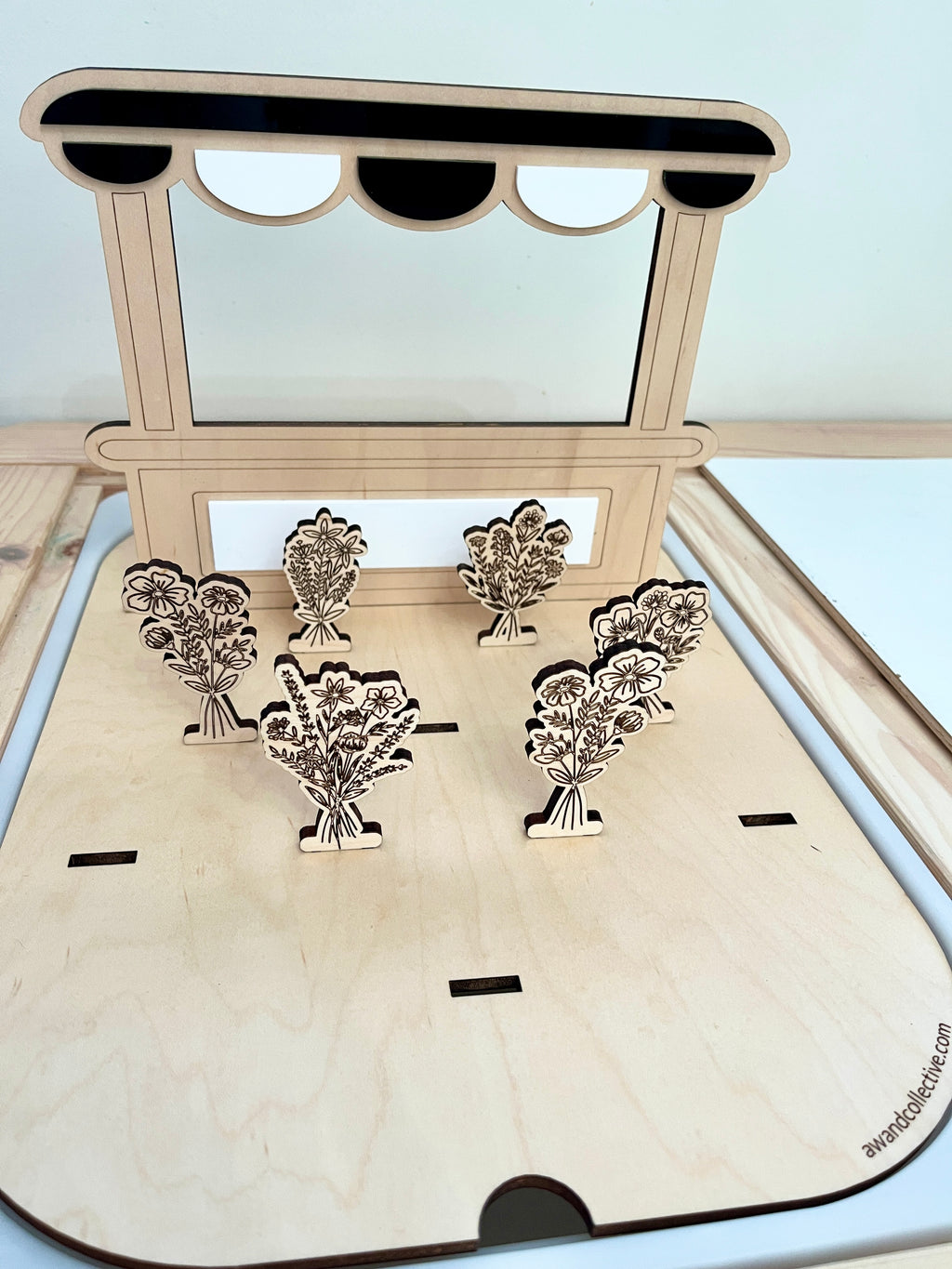 Laser-cut wooden flower bouquets displayed on a small stand with a scalloped canopy on a light wood base
