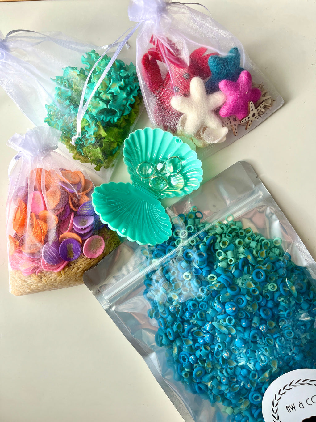 Assorted sensory materials including felt sea stars, green coral, colorful shells, blue ring beads, and a teal clam container.