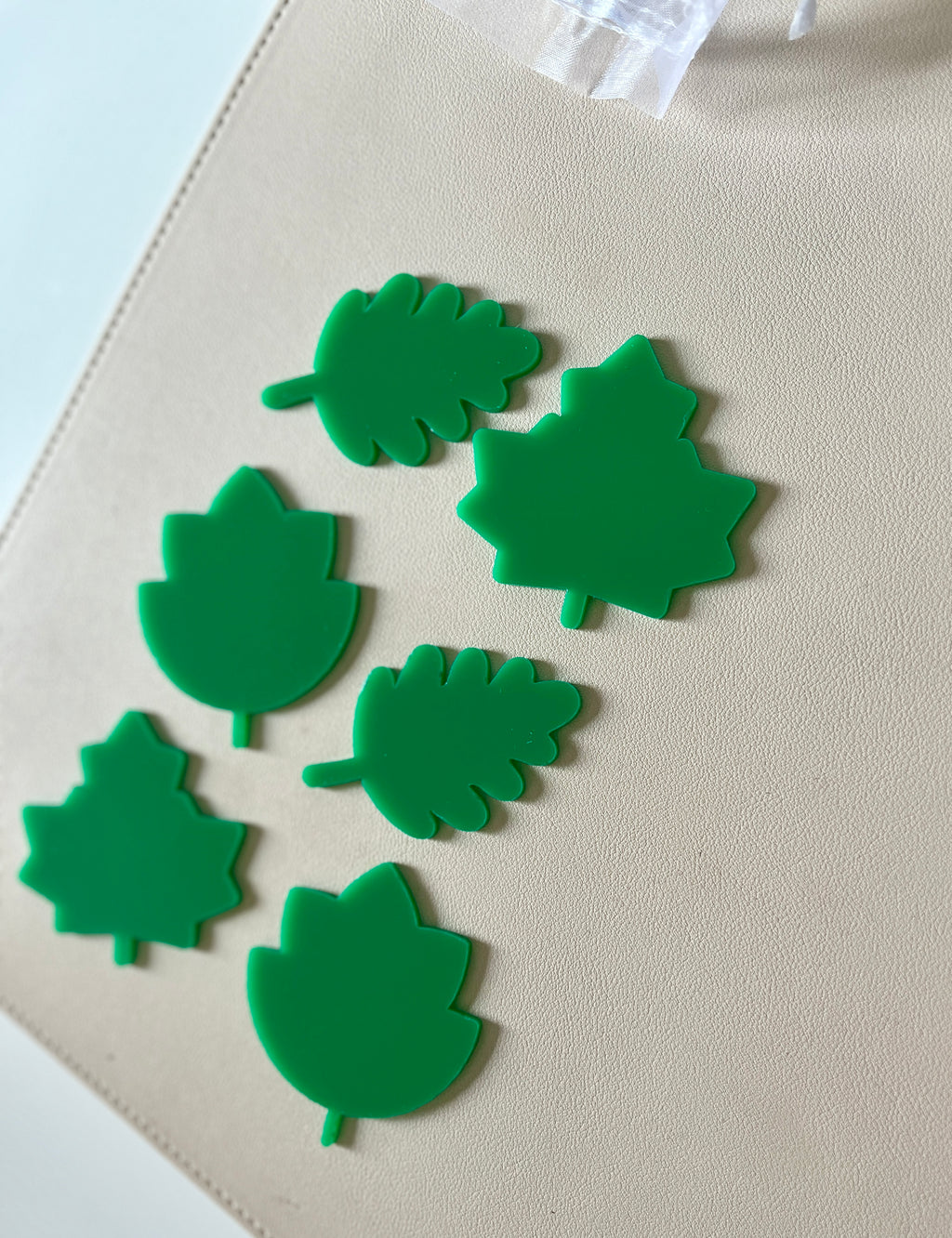 Six bright green plastic leaf-shaped cutouts of various designs arranged on a beige surface