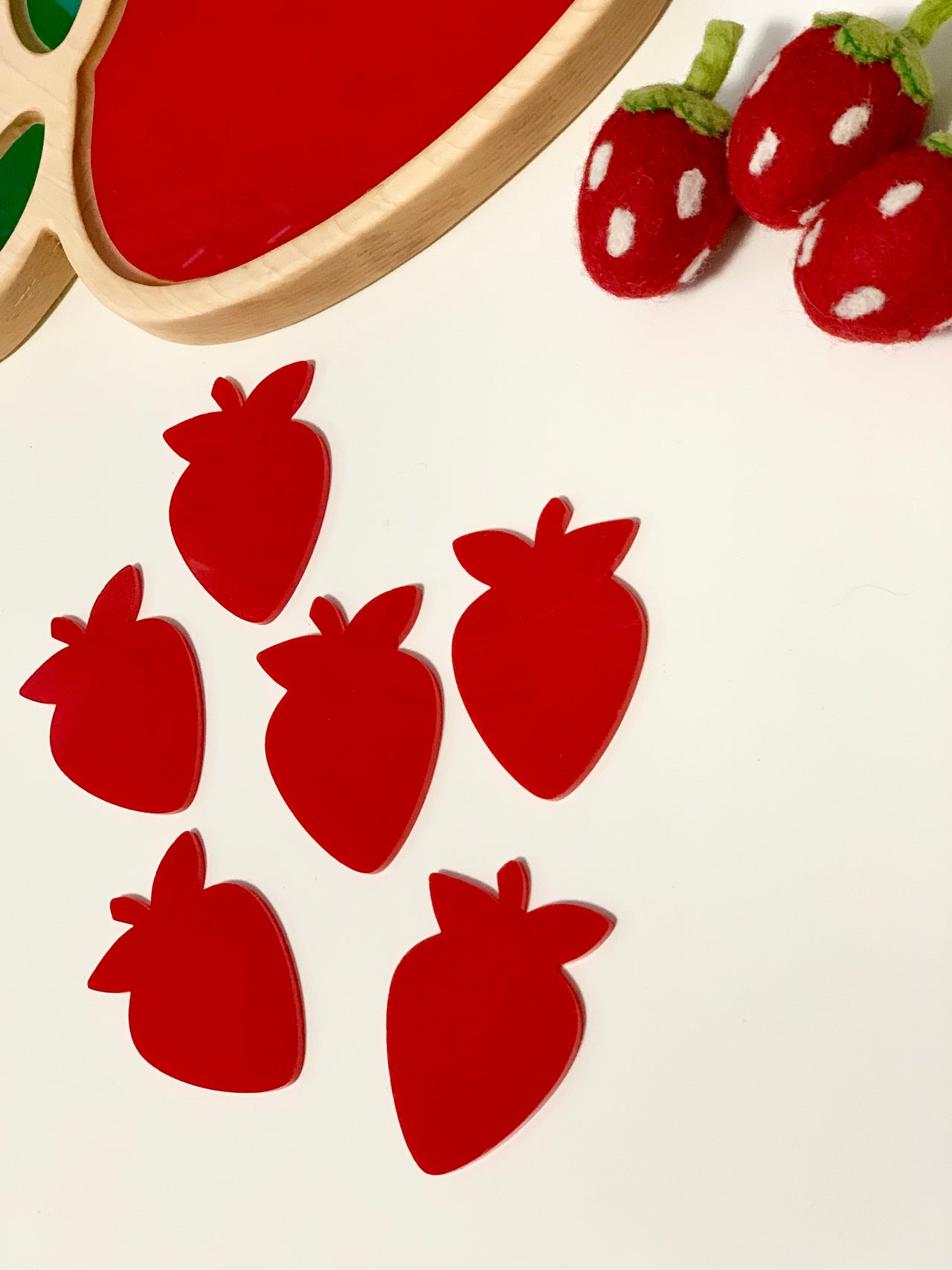 Set of six red strawberry-shaped dry erasable boards with wooden tray and felt strawberry toys on white surface