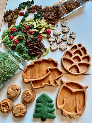 Set of three wooden mini woodland trays shaped like a hedgehog, owl, and pinecone with natural play pieces on white surface