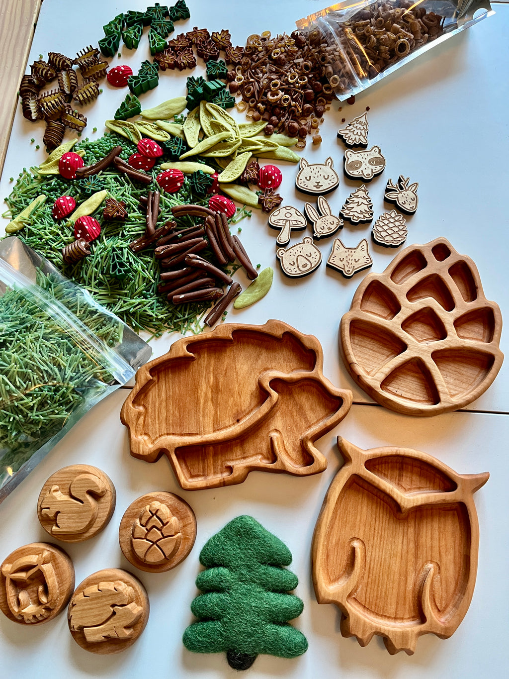 Set of three wooden mini woodland trays shaped like a hedgehog, owl, and pinecone with natural play pieces on white surface