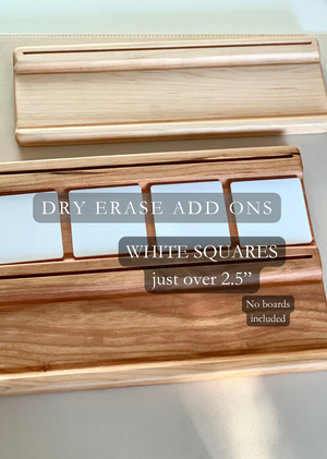 Two wooden dry erase marker holders with slots for white square dry erase add-on pieces on a light surface