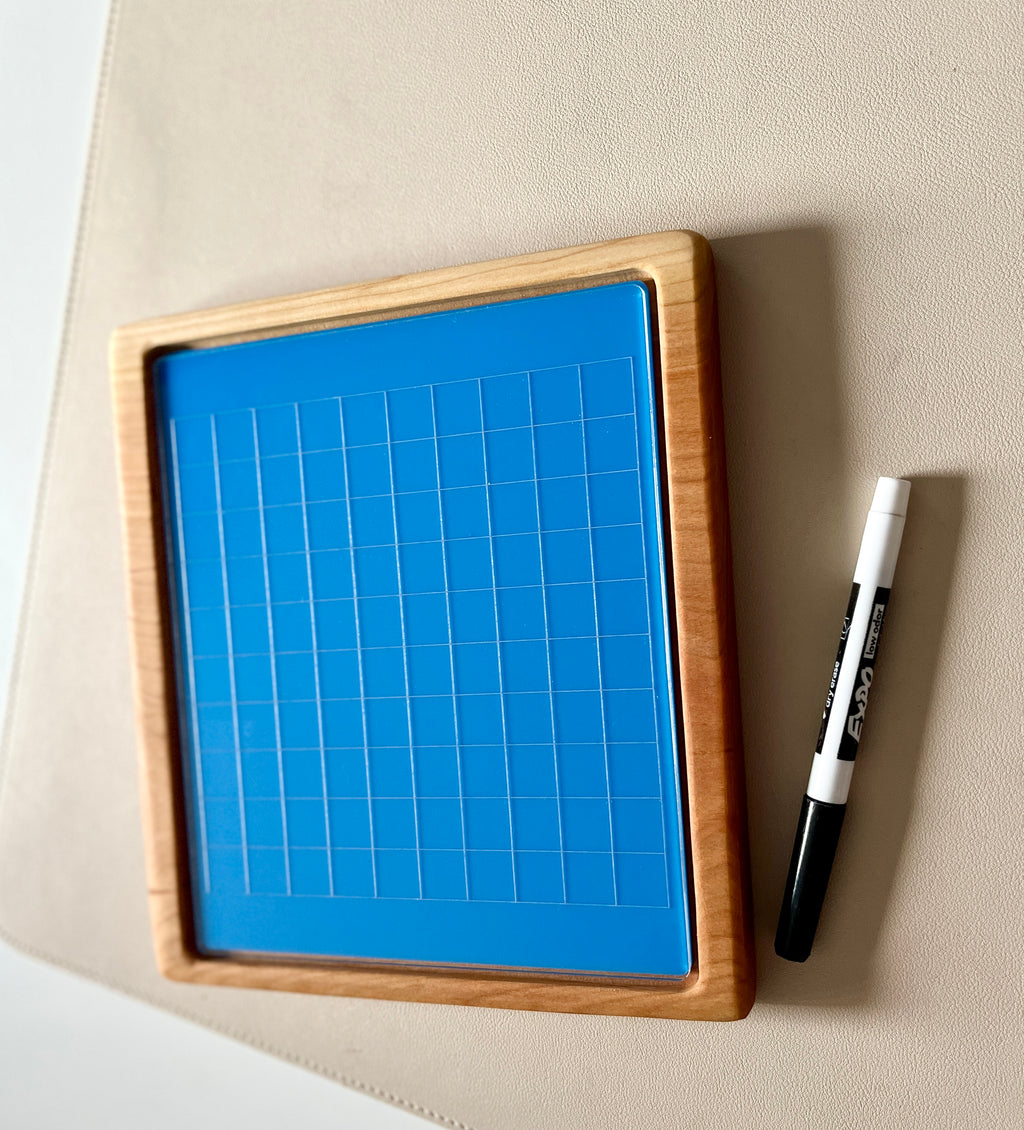 Wooden-framed blue magnetic board with grid lines next to a black and white dry erase marker on beige surface
