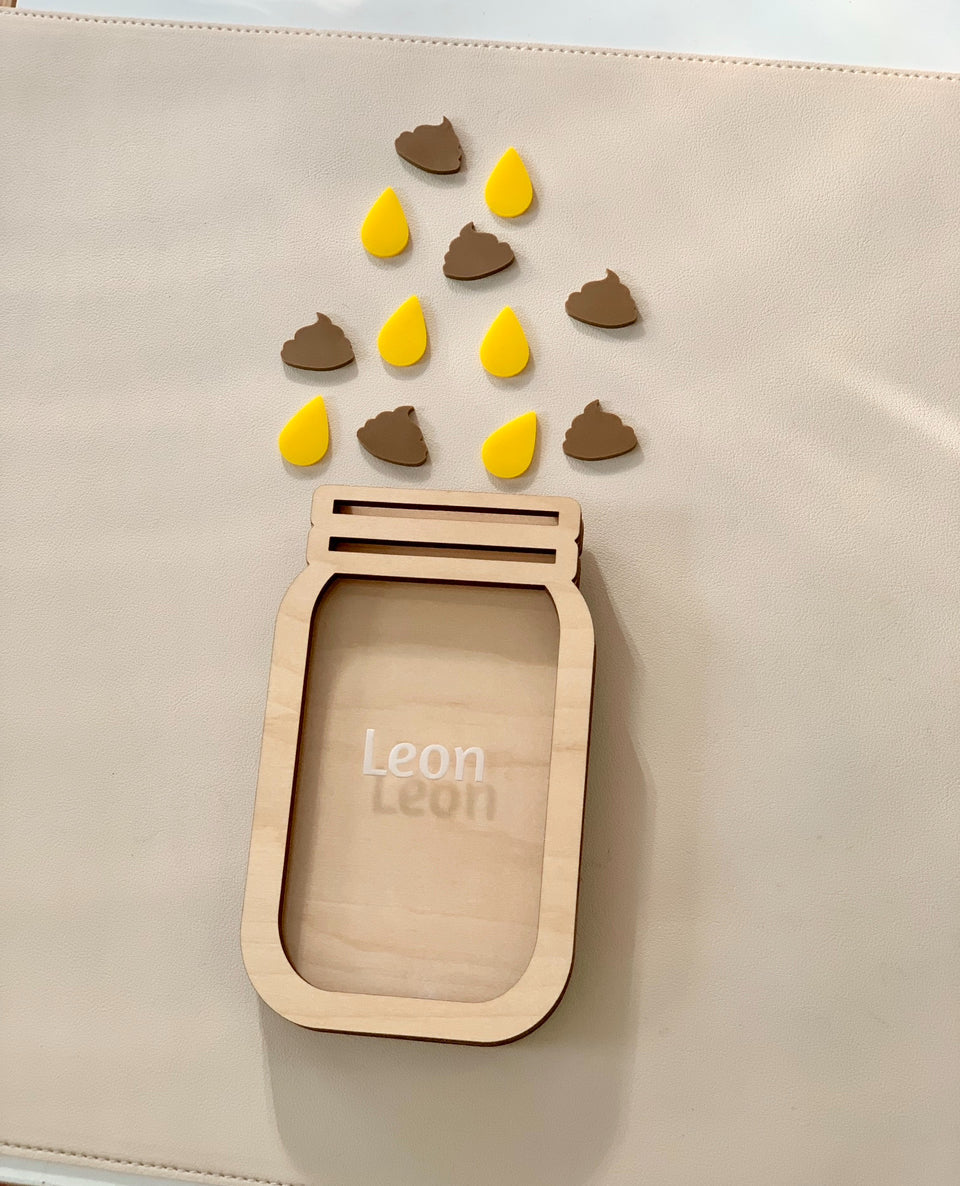Light wooden jar-shaped frame personalized with the name Leon and scattered yellow teardrop and brown poop tokens above on beige surface