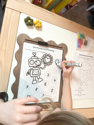 Child tracing a robot picture on a dry erase insert in a nice wooden tray with markers.