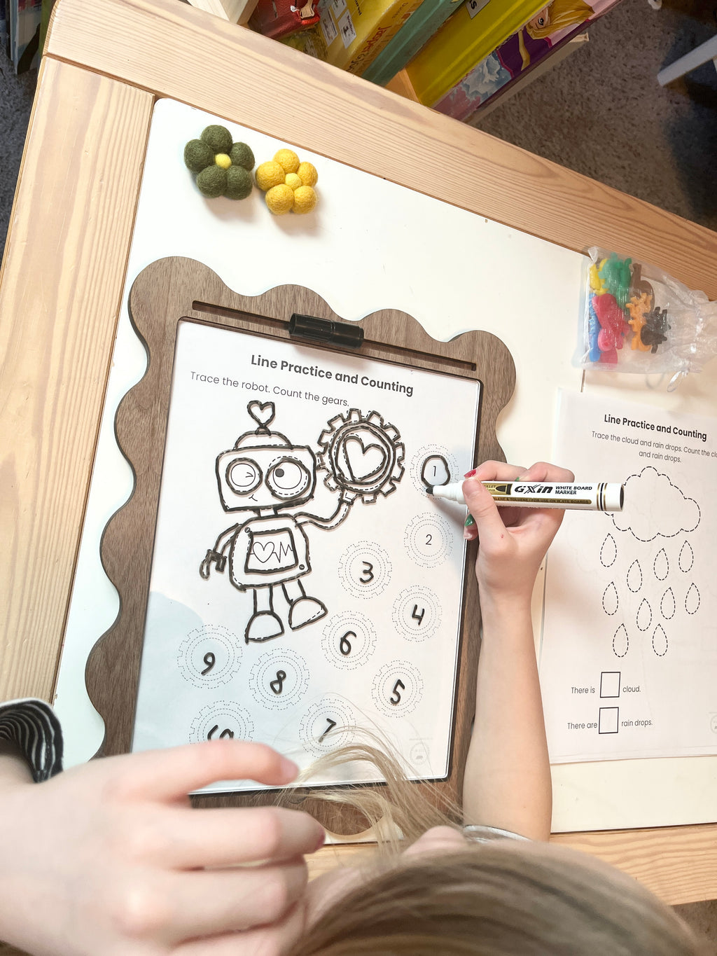 Child tracing a robot picture on a dry erase insert in a nice wooden tray with markers.