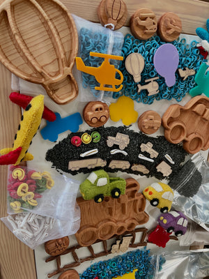 Assorted wooden vehicle shapes, colorful felt cars, and craft supplies arranged on a wooden table surface.