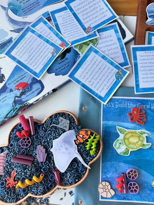 Cloud-shaped wooden sensory tray filled with black rice, colorful sea creature toys, and ocean-themed activity cards