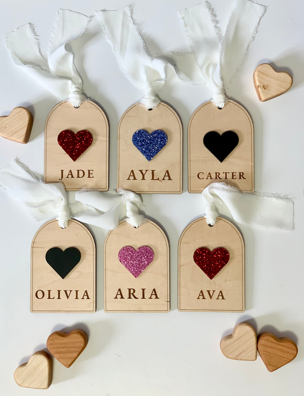 Set of six wooden gift tags with glittery and solid heart shapes and engraved names tied with white fabric ribbons