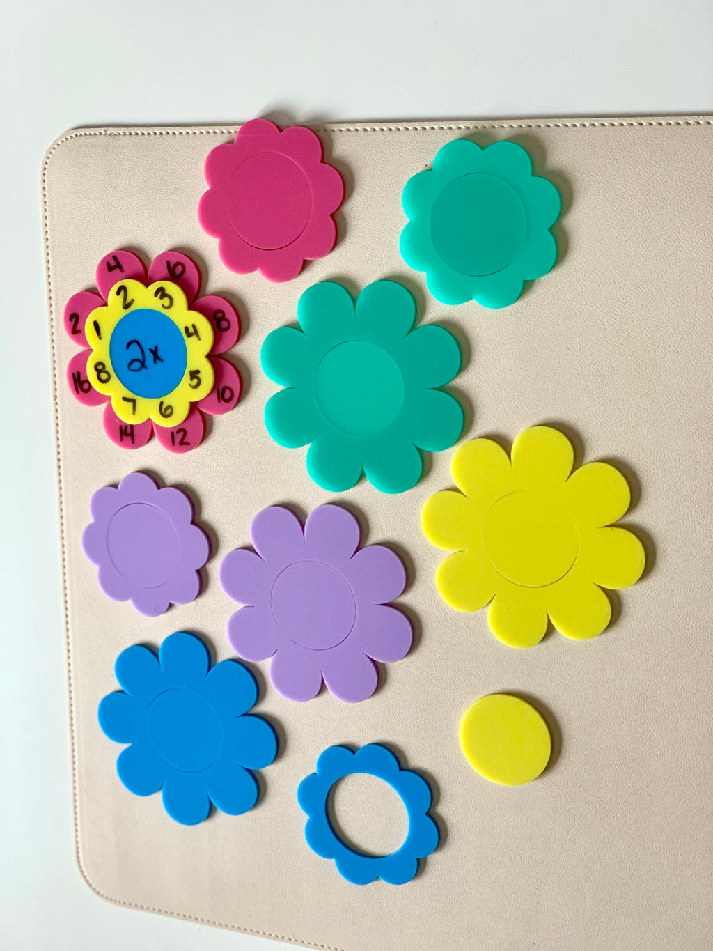 Assorted colorful plastic flower-shaped pieces and a yellow circular disk arranged on a beige surface