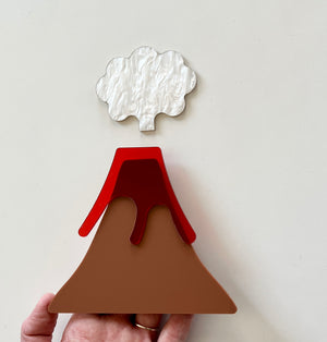 Hand holding layered acrylic volcano shape with brown base, red lava, and white cloud on white background