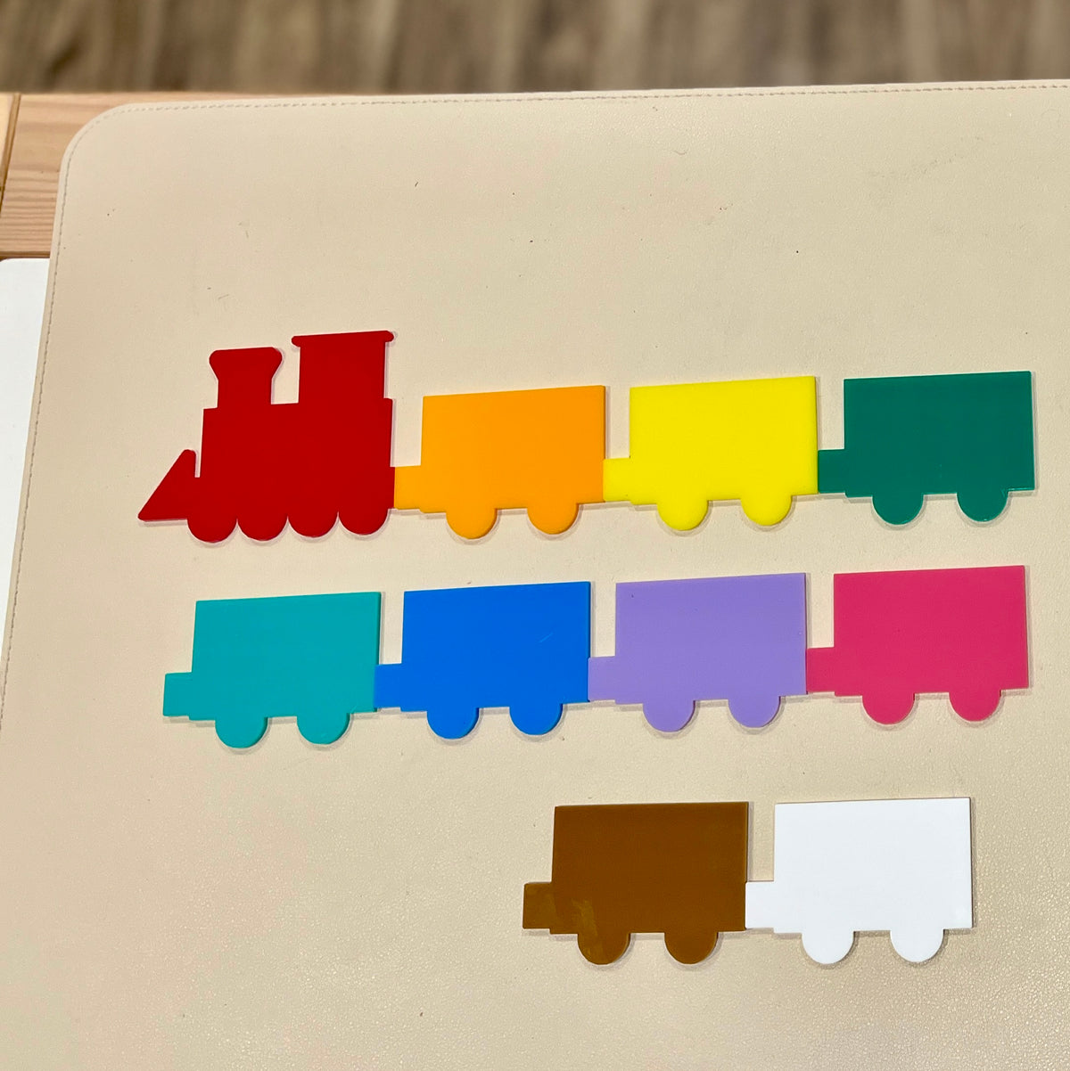 Multicolored flat train engine and cars in red, orange, yellow, green, blue, purple, pink, brown, and white on a light surface