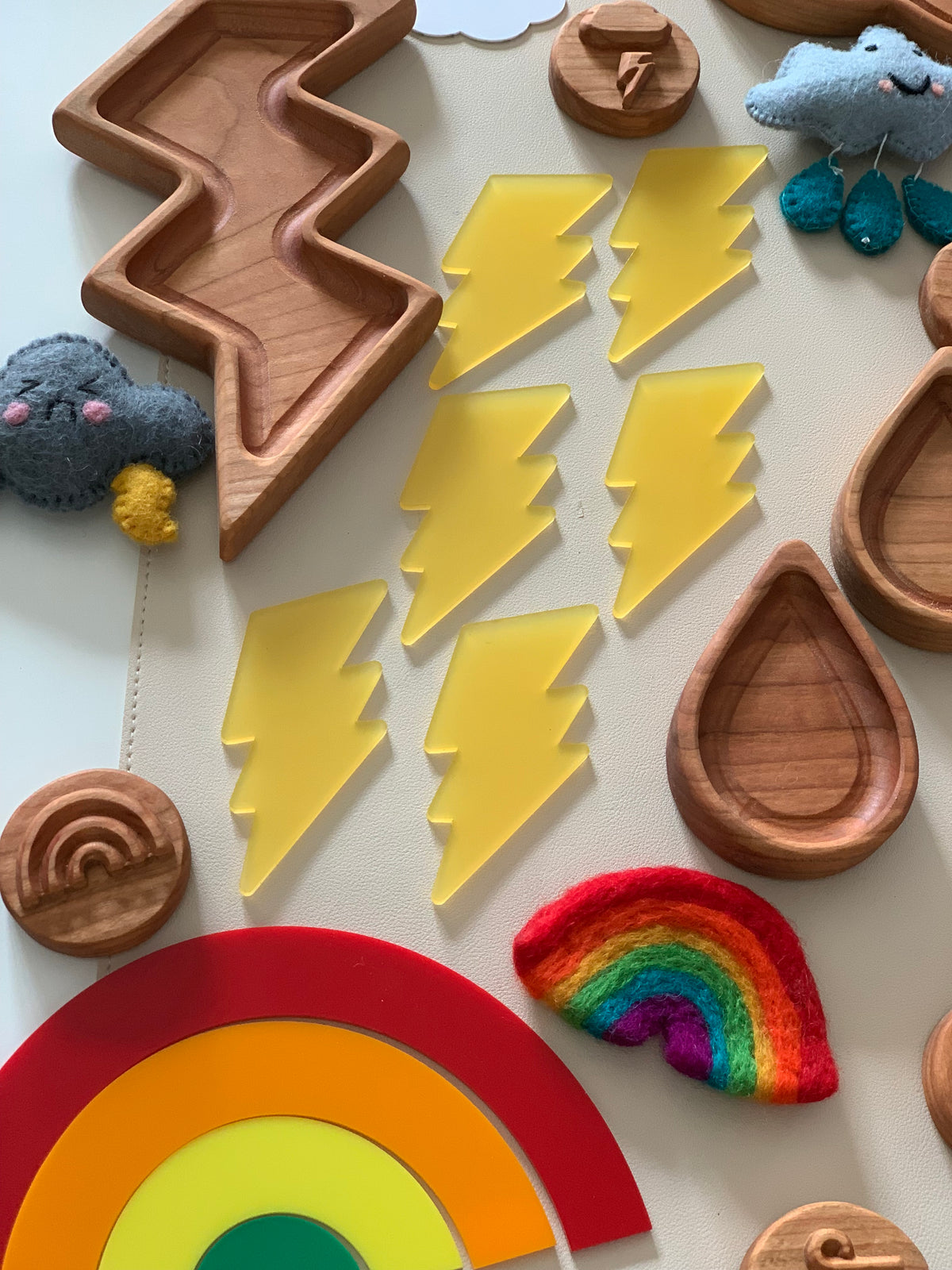 Seven translucent yellow lightning bolt shapes arranged beside wooden trays and colorful felt weather figures on a white surface