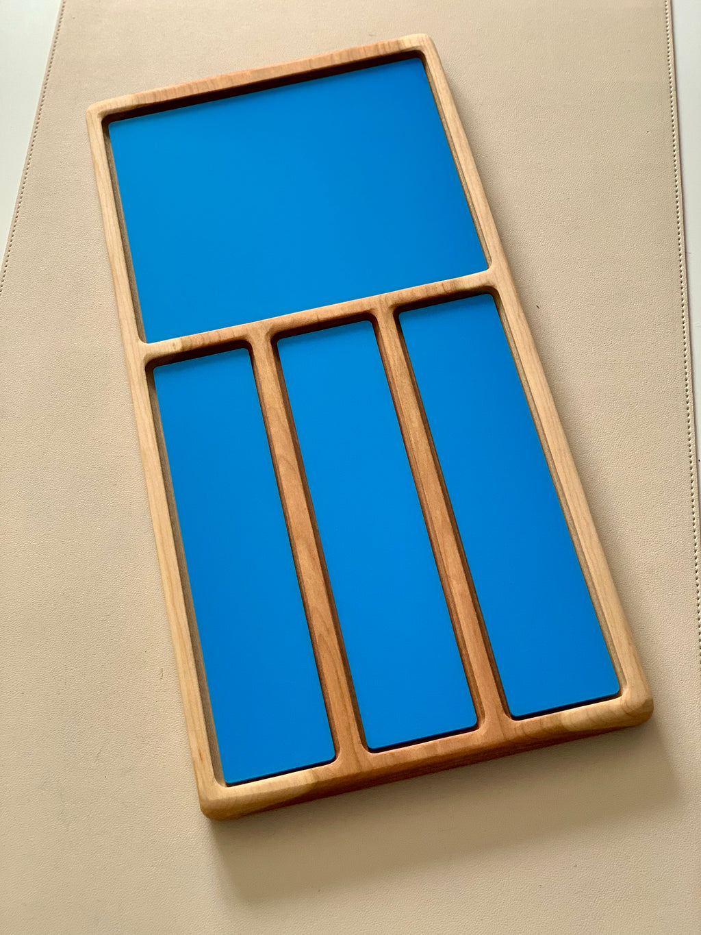Wooden organizer tray with one large compartment and three narrow blue rectangular sections on a beige surface