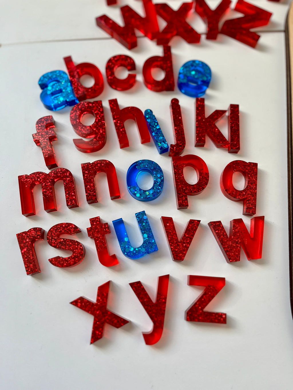 Lowercase resin letters in bright red with glitter and blue letters with confetti scattered on a white surface