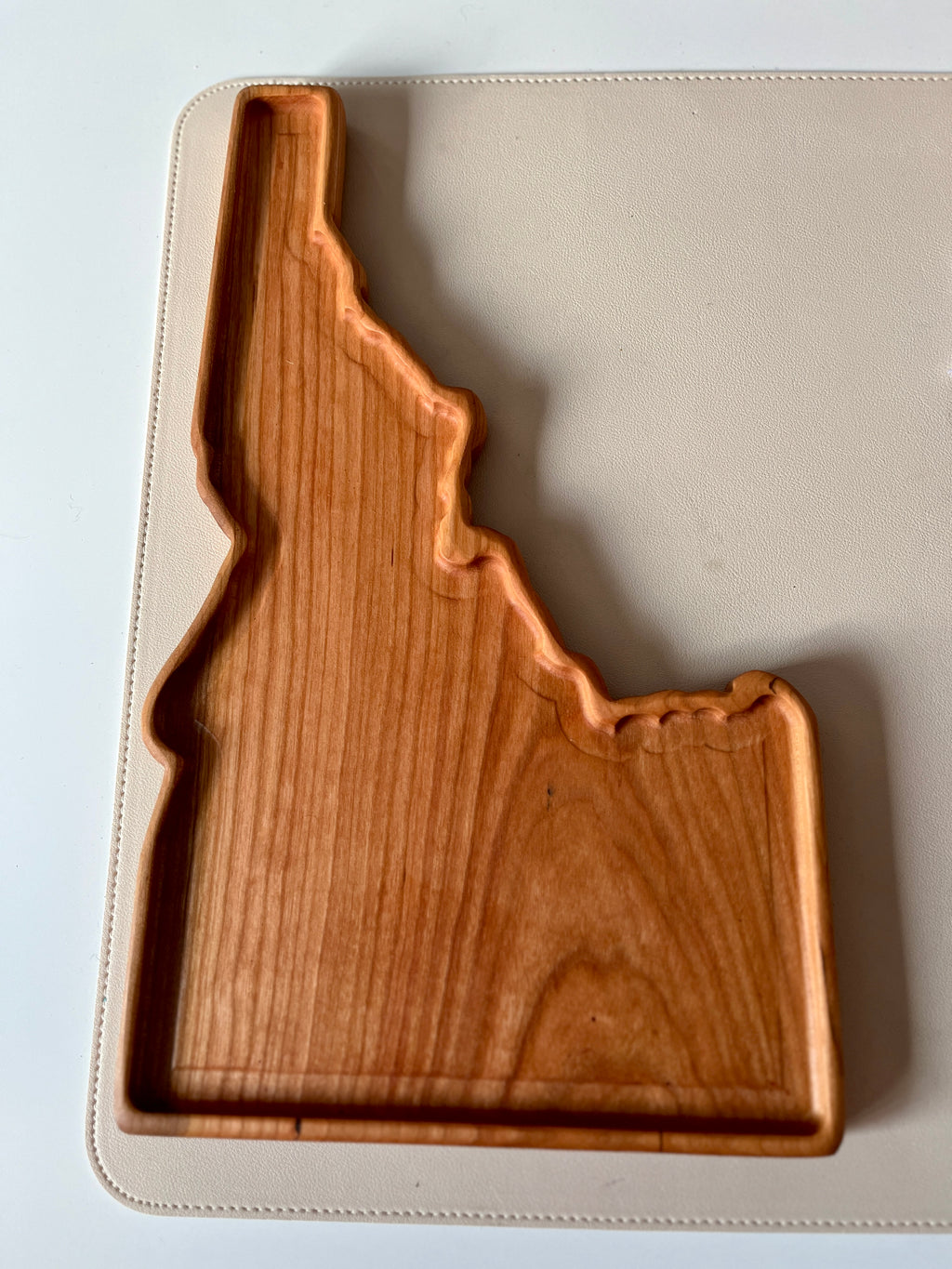 Handcrafted wooden tray shaped like Idaho with natural wood grain on a beige textured surface