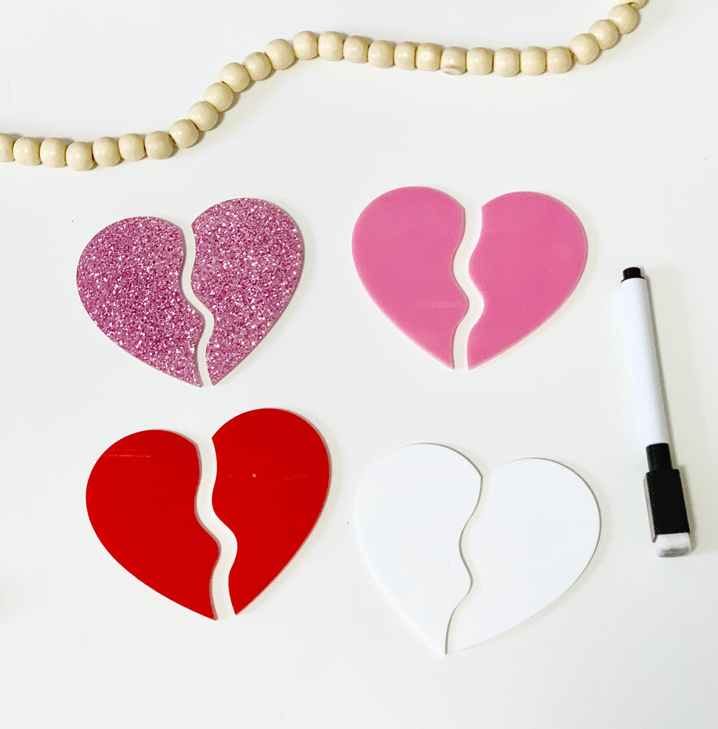 Four broken heart-shaped boards in glittery pink, solid pink, red, and white with a black dry erase marker on white surface