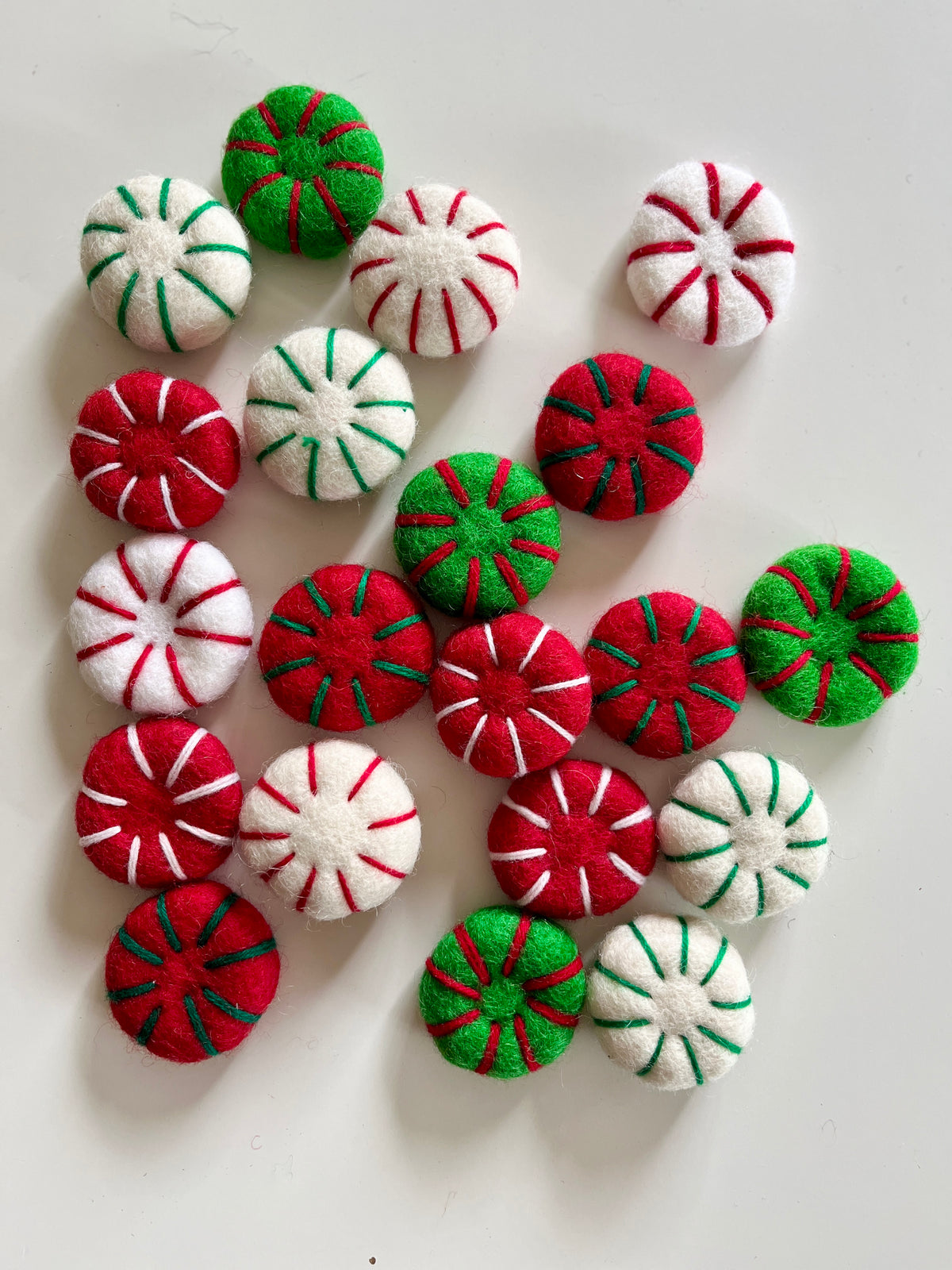 Assorted round felt decorations in red, green, and white with contrasting stitched stripes scattered on white surface