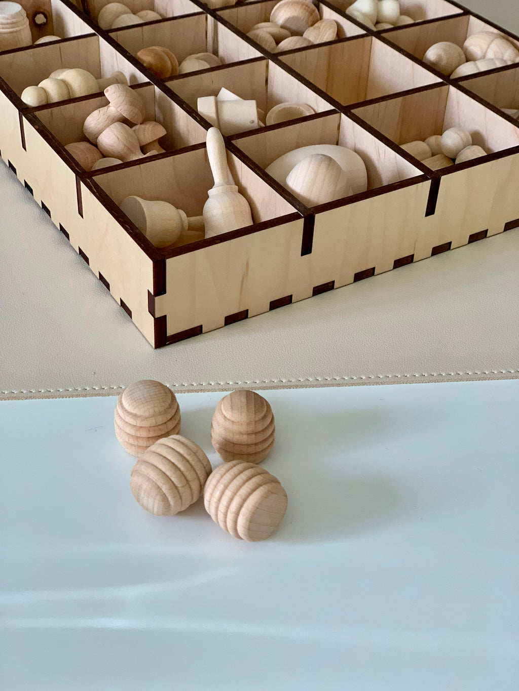 Smooth unfinished wooden beads and shapes organized in a divided wooden storage box on a light surface