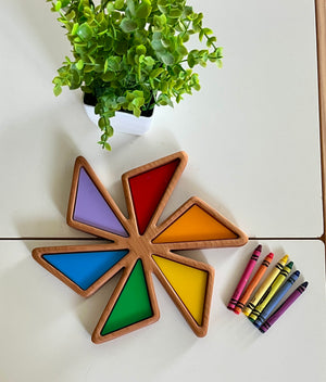 Star-shaped wooden tray with colorful triangular compartments beside a set of crayons and a small green potted plant