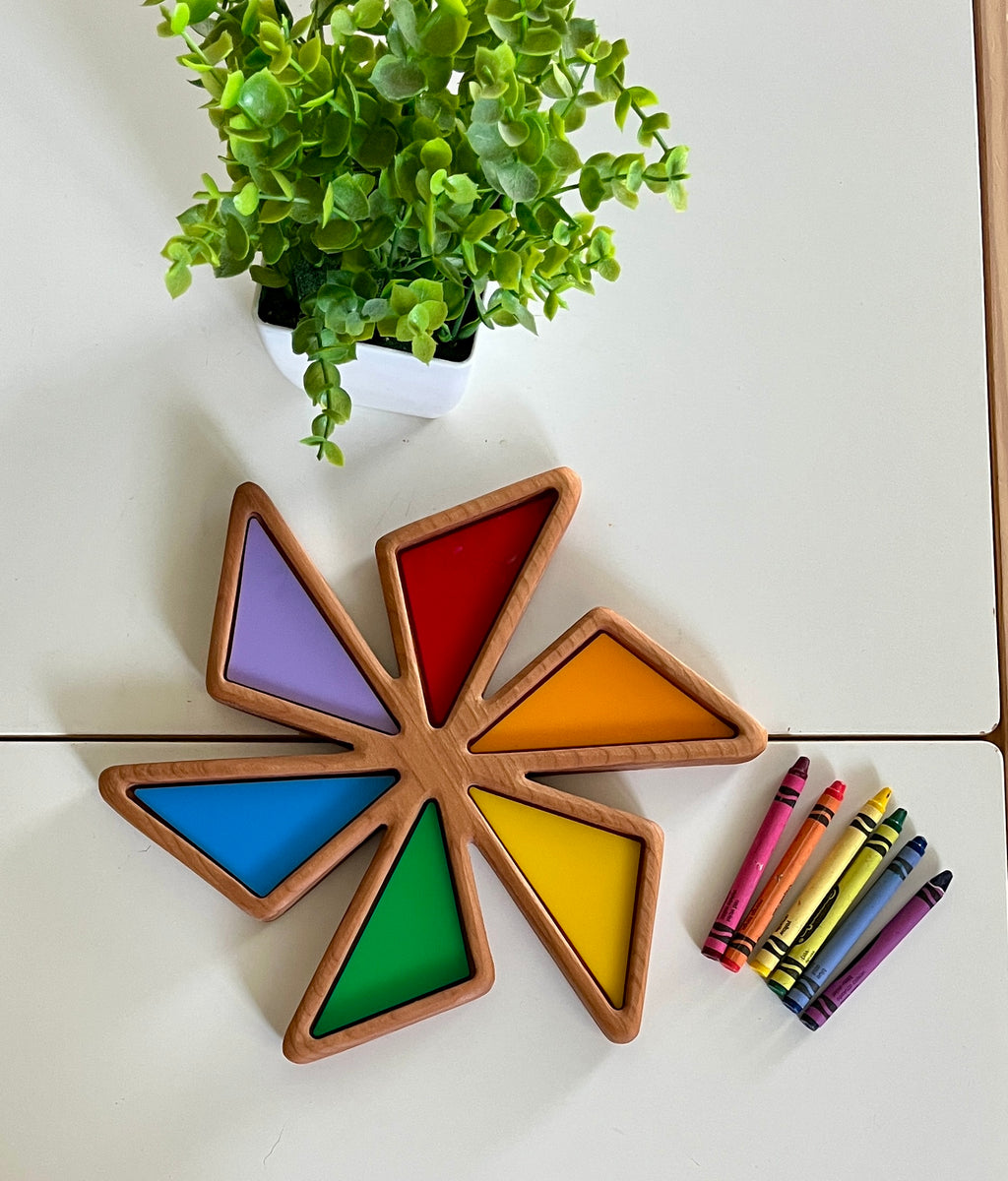 Star-shaped wooden tray with colorful triangular compartments beside a set of crayons and a small green potted plant