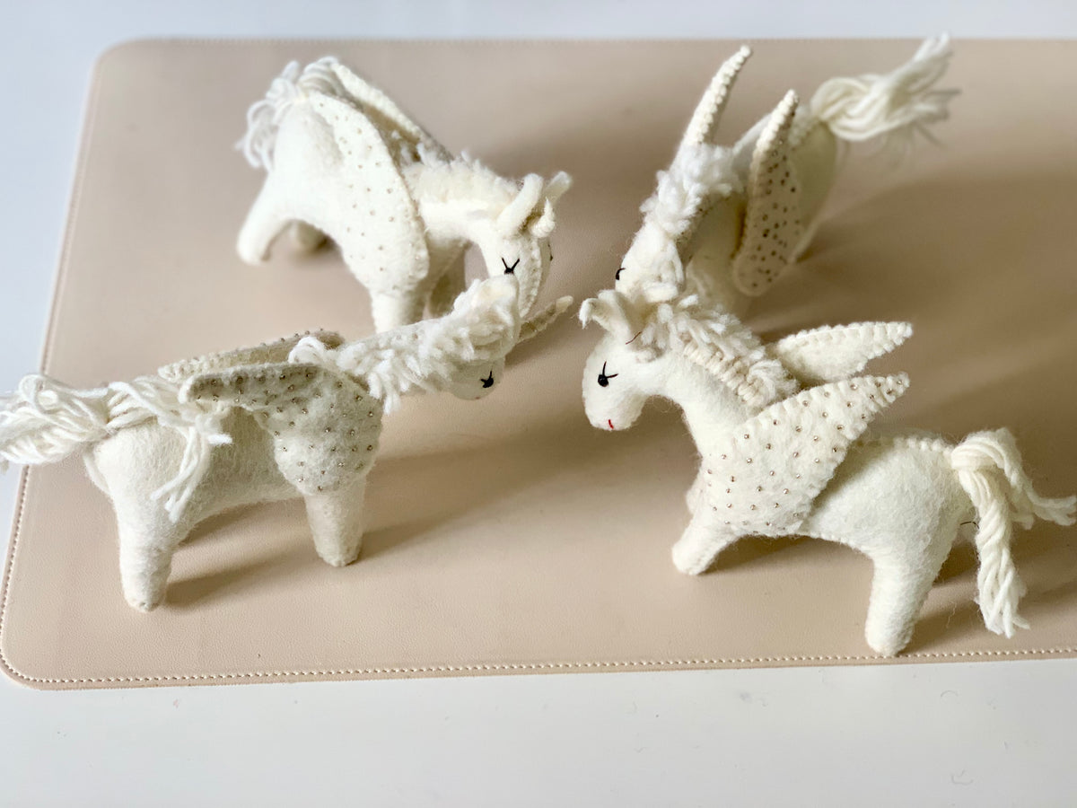 Four handmade white felt donkey dolls with textured details and braided tails arranged on a beige surface