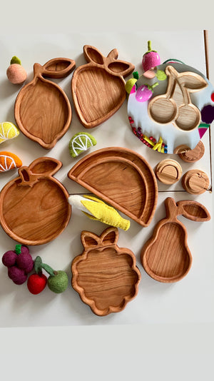 Assorted wooden fruit-shaped trays including lemon, strawberry, apple, watermelon, grape, and pear with colorful felt fruit decorations