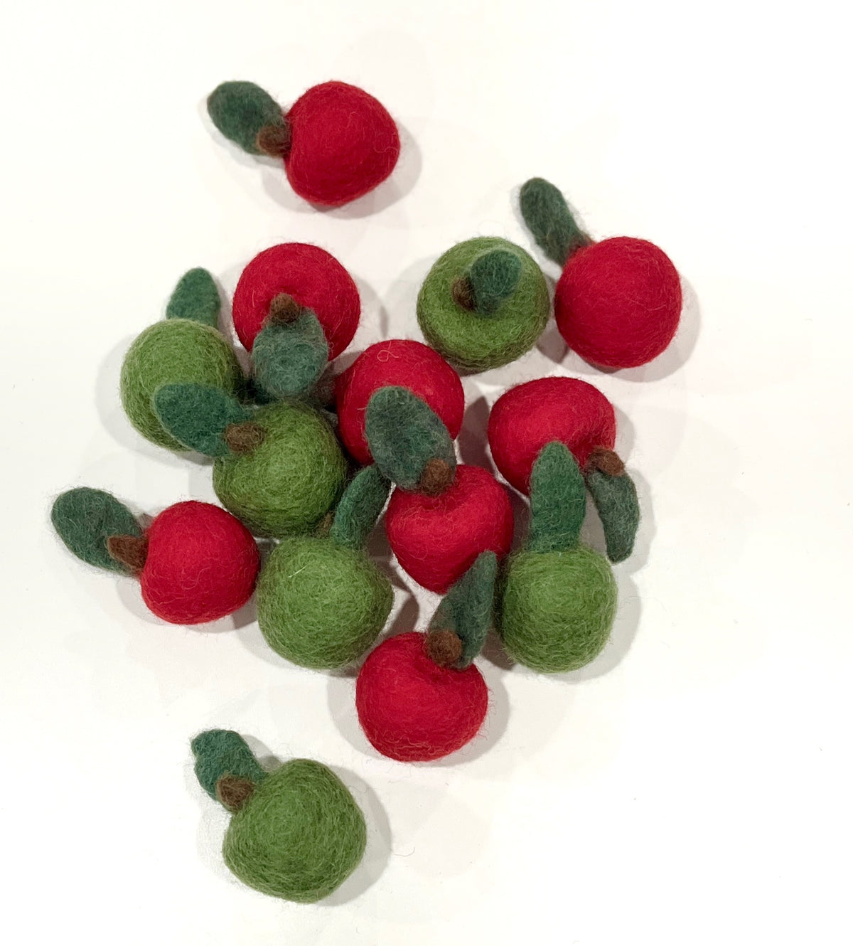 Small red and green wool felt berries with attached green leaves scattered on a white background