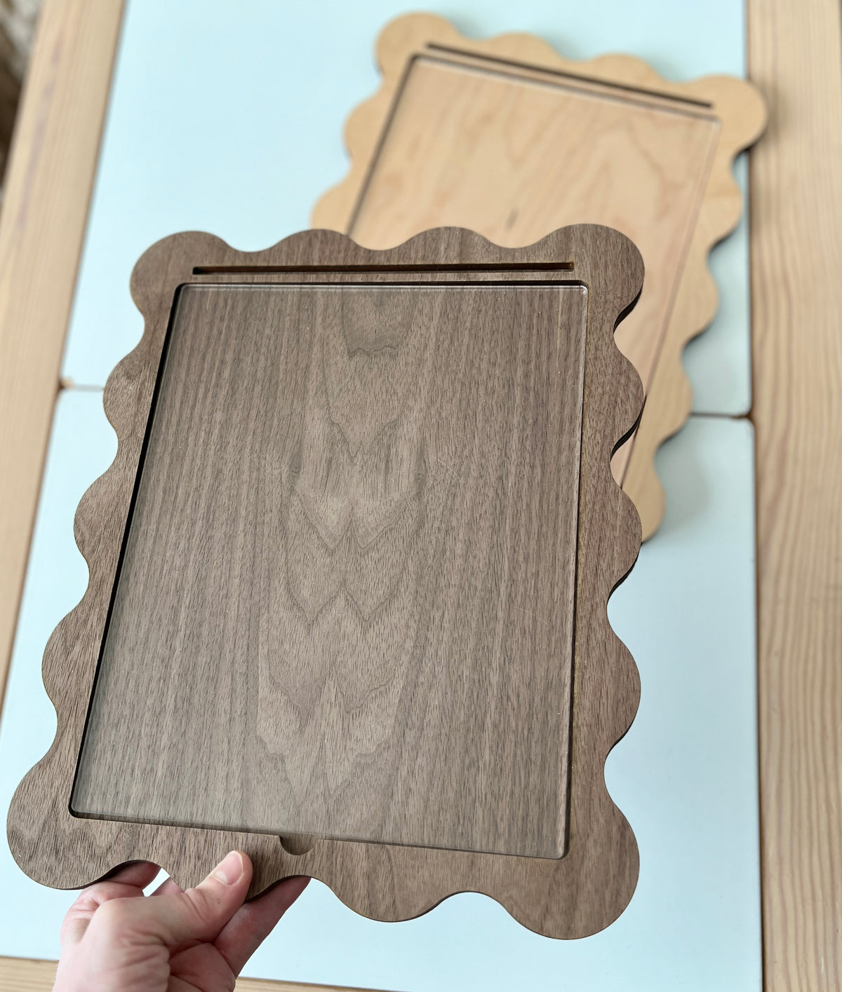 Hand holding a Walnut Laser Cut Writing Sensory Tray for 8.5 x 11 sheets with Dry Erase Inserts and Slot for Acrylic - Scalloped Design, made from rich walnut wood, handcrafted homeschool educational resources.