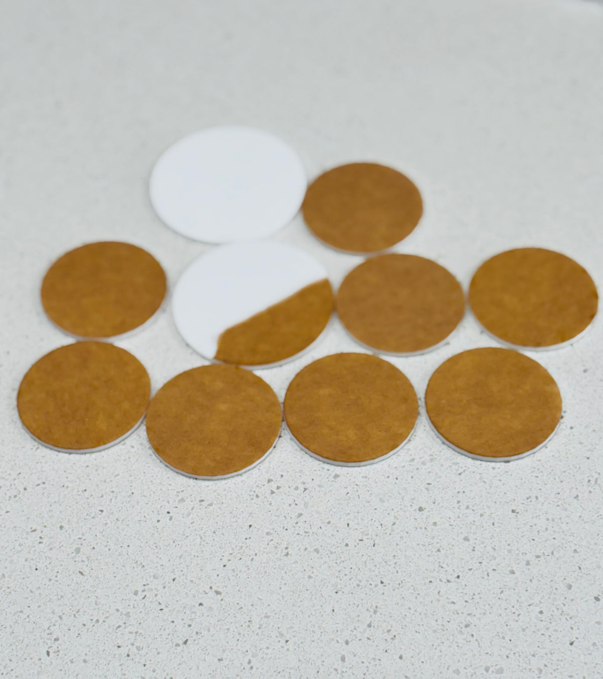 Round leather and white felt coasters arranged loosely on a light textured surface