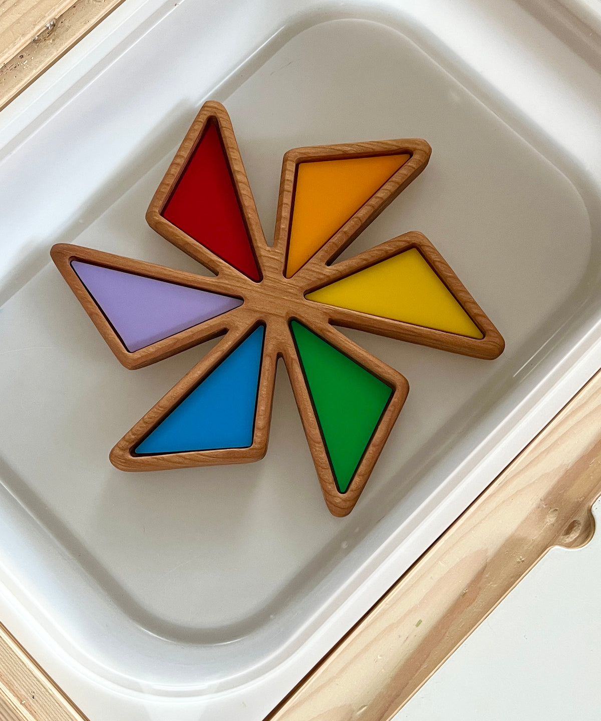 Wooden star-shaped tray with six colorful triangular sections in red, orange, yellow, green, blue, and purple on a white surface