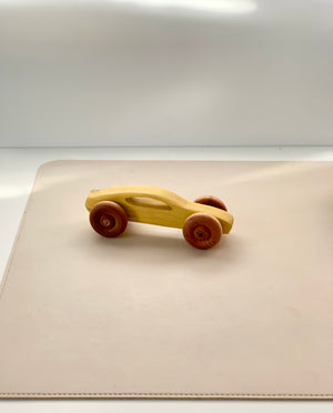 Smooth wooden toy car with rounded red wheels on a soft beige surface in natural light