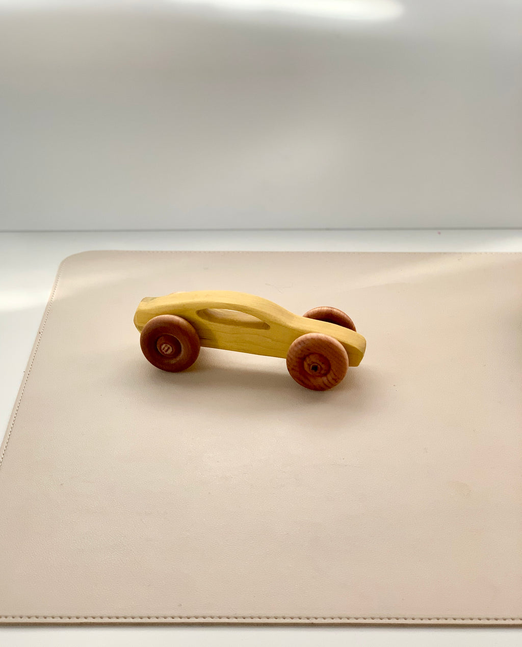 Smooth wooden toy car with rounded red wheels on a soft beige surface in natural light