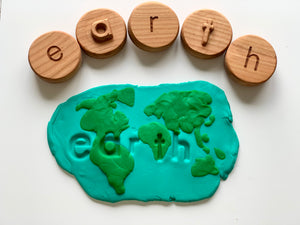 Wooden letter tokens spelling "earth" above blue and green playdough shaped like a world map with the word earth embossed