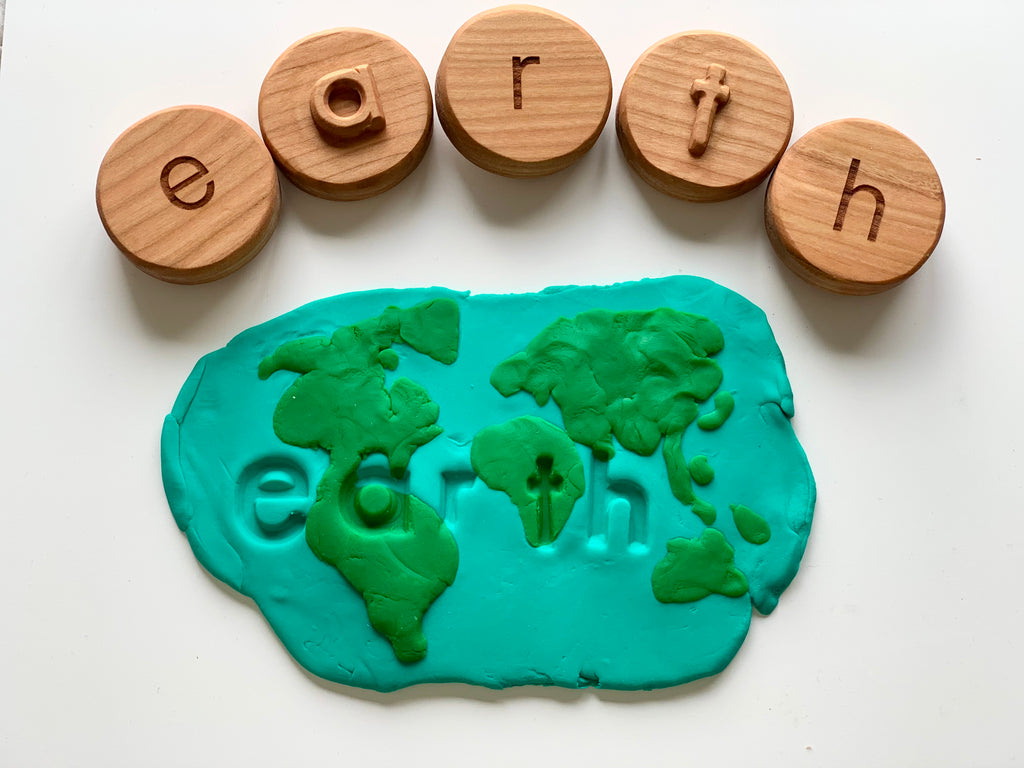 Wooden letter tokens spelling "earth" above blue and green playdough shaped like a world map with the word earth embossed