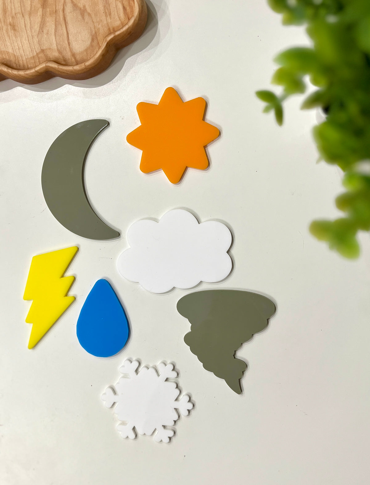 Assorted colorful weather-themed shapes including sun, moon, cloud, lightning bolt, raindrop, tornado, and snowflake on a white surface