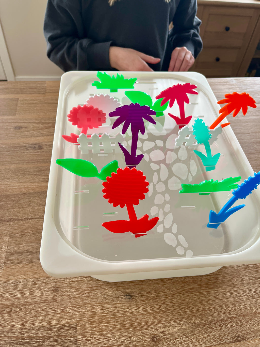 White tray with a stone path design holding colorful translucent acrylic pegs in various plant and garden shapes, showcasing STEM Insert – Acrylic Insert with Different Peg Options - Neighborhood, Veggie Garden, Flower Garden, Under the Sea + More, handcrafted, homeschool, education resources.