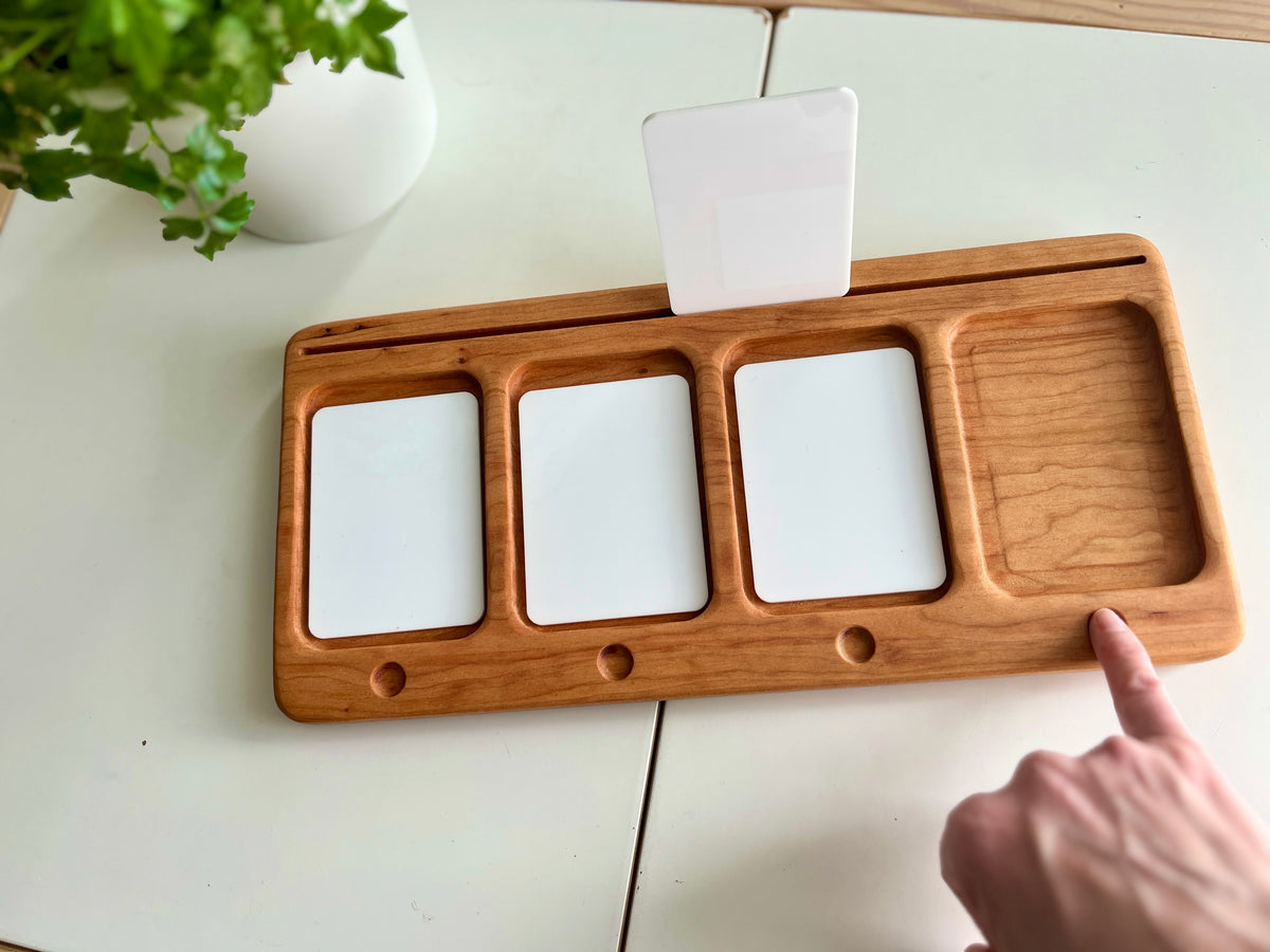 Wooden organizer tray with three white slots, a small rectangular compartment, and a white card held upright on a white table