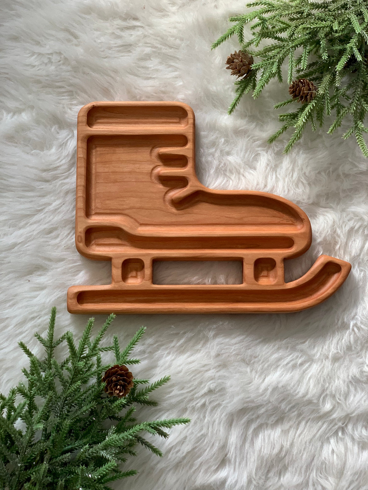 Wooden skate-shaped sensory tray with carved compartments on soft white fur surrounded by pine branches and cones