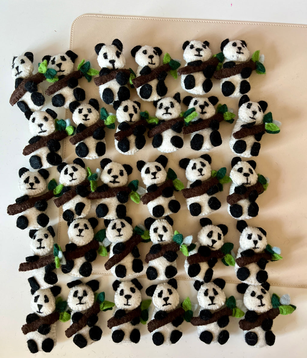 Rows of small felt pandas with black and white markings holding brown branches adorned with green leaves on a beige surface