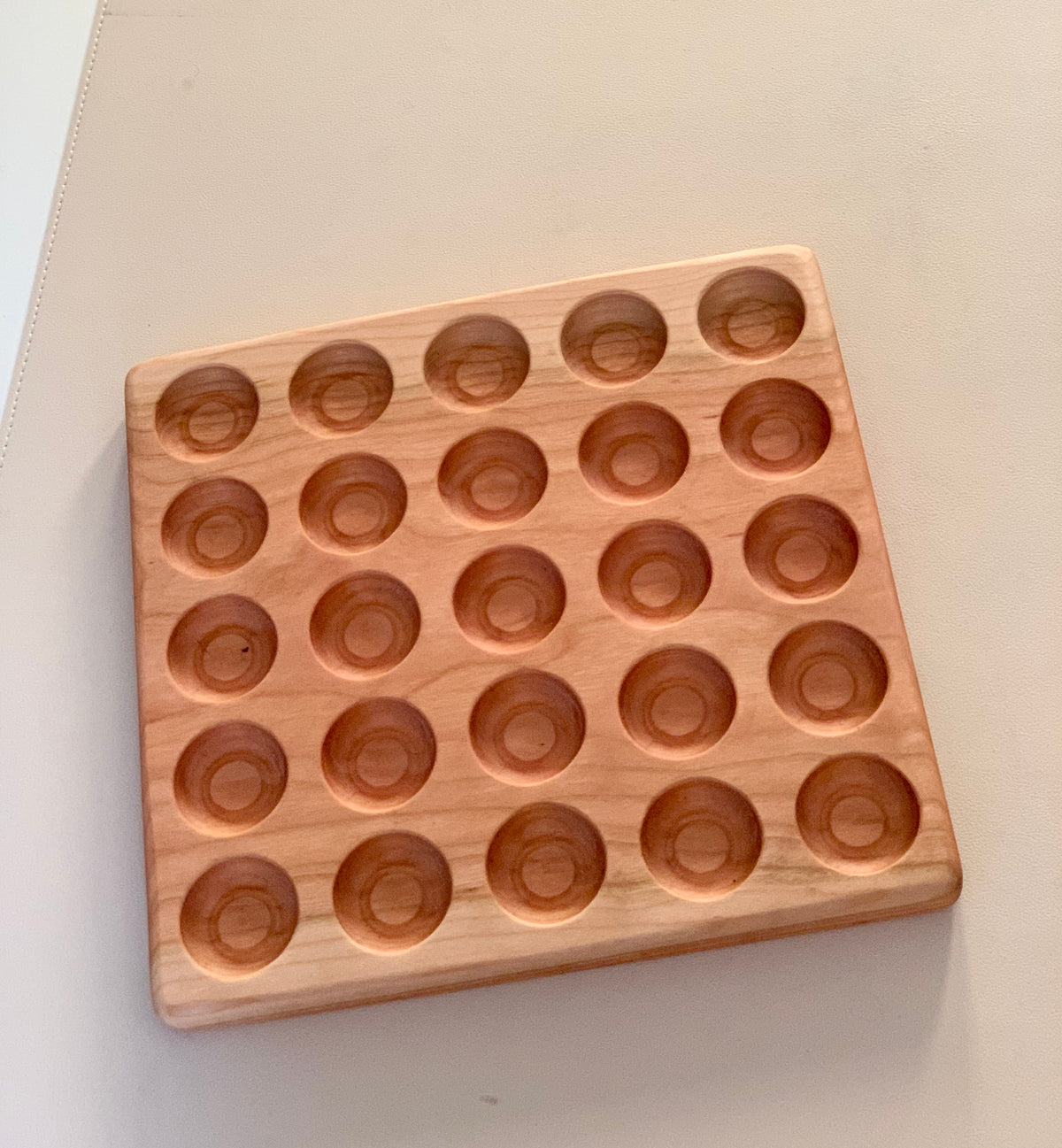 Square wooden board with five rows of circular indentations on a neutral surface