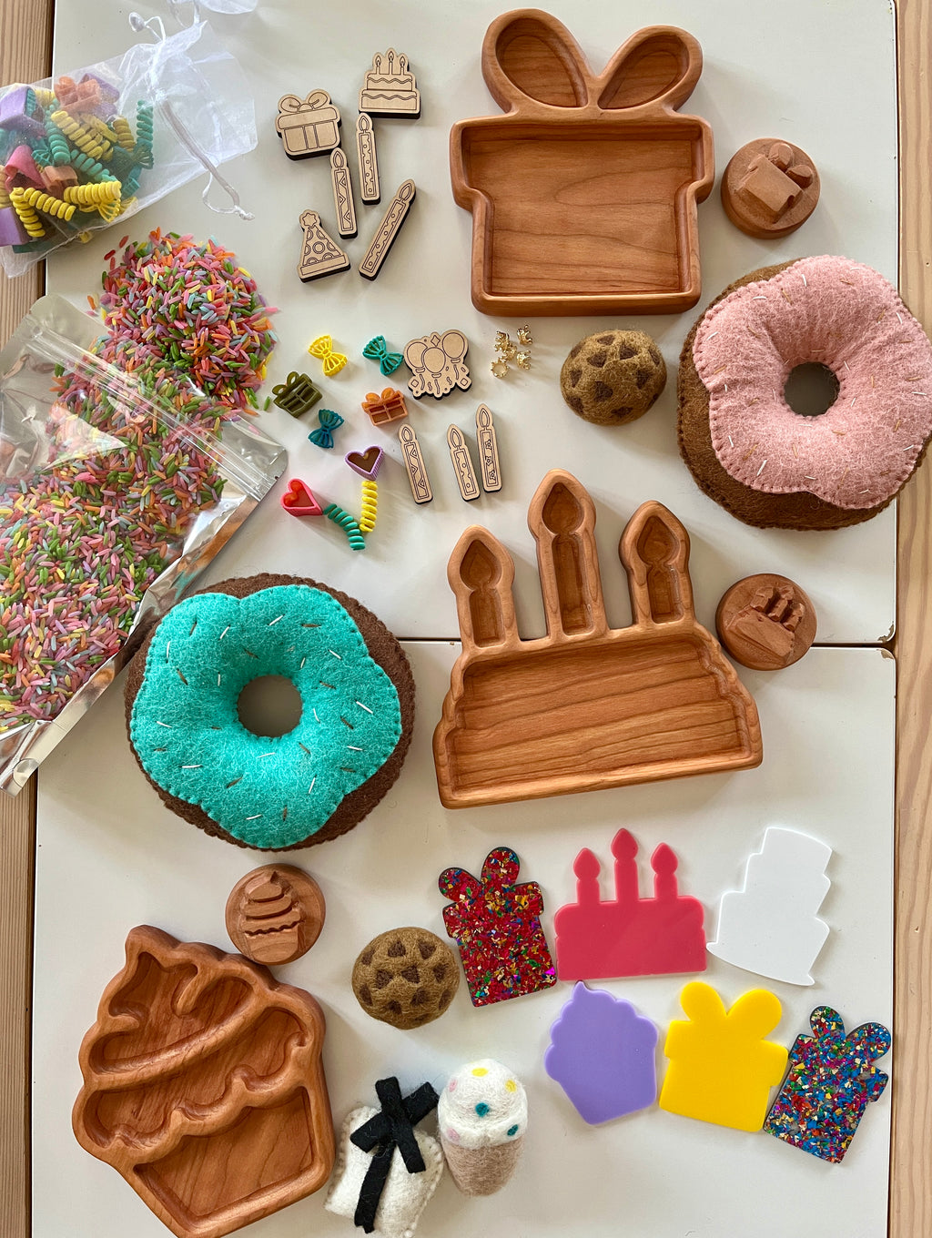 Wooden trays shaped like gift, cake, and cupcake surrounded by colorful felt sweets, sprinkles, and miniature decorations