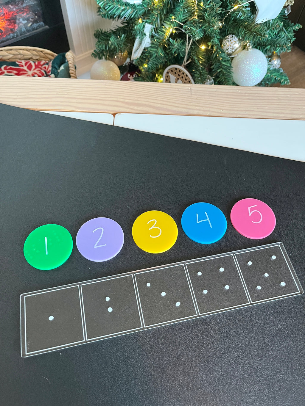 Black surface with five colorful discs numbered 1 to 5 above outlined dice dots in five boxes