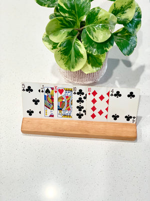 Extra long wooden flash card holder displaying playing cards with green plant in woven pot background