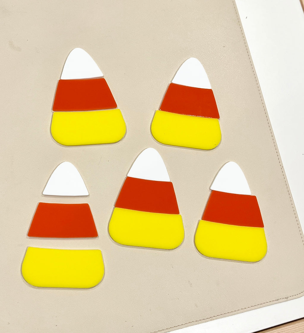 Five three-layered candy corn shapes in white, orange, and yellow arranged on a beige surface