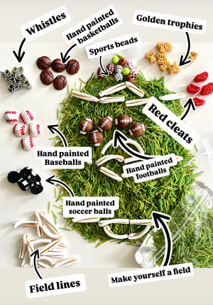 Assorted sports-themed miniature items including hand painted balls, whistles, red cleats, golden trophies, and field lines on faux grass