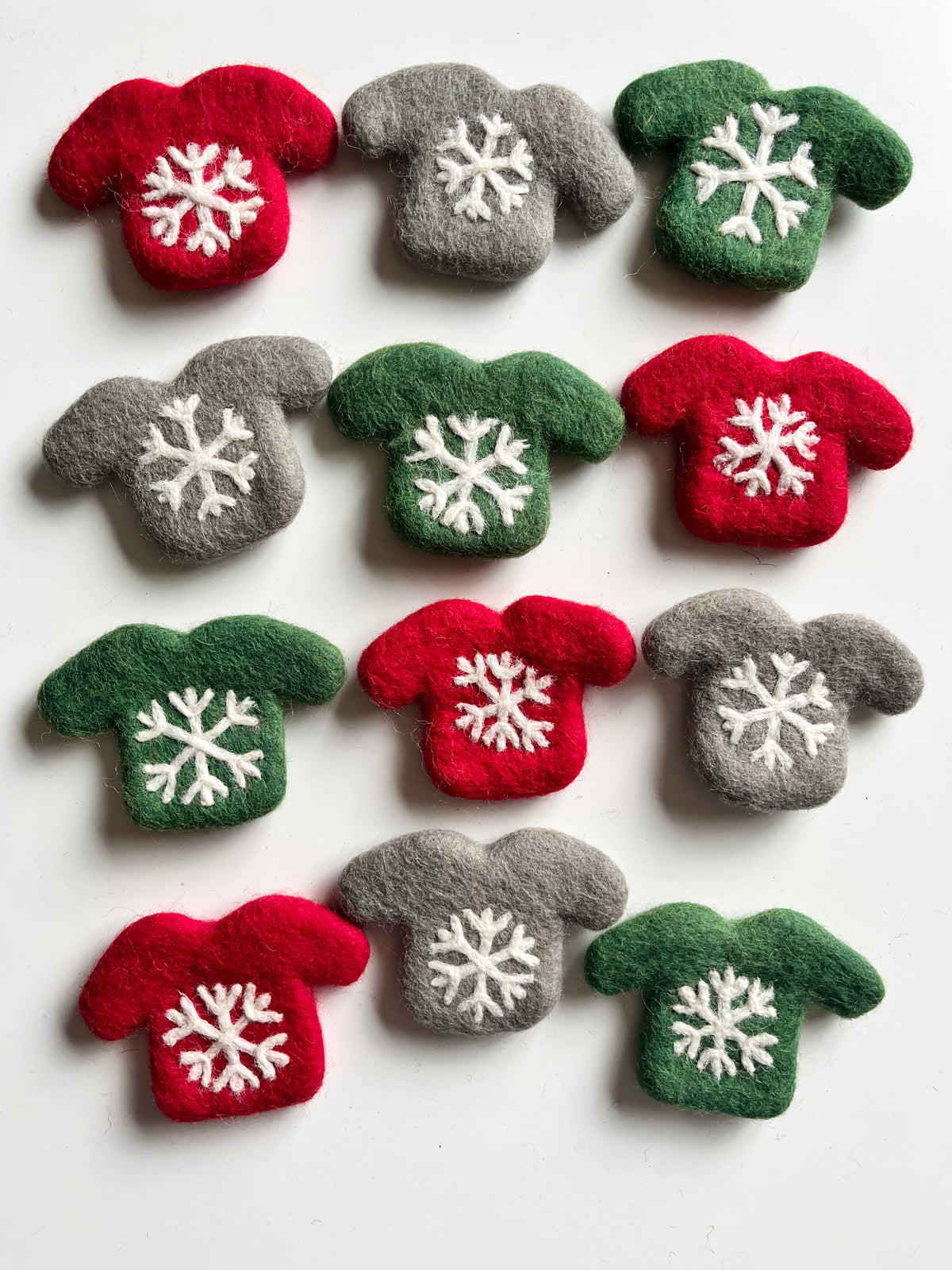 Assorted red, green, and gray felt mini sweaters with white stitched snowflake patterns on white background